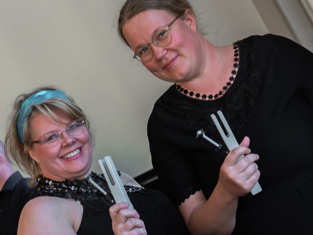 Kaksi hymyilevää naista katsoo kameraan ja pitää käsissään soittimia