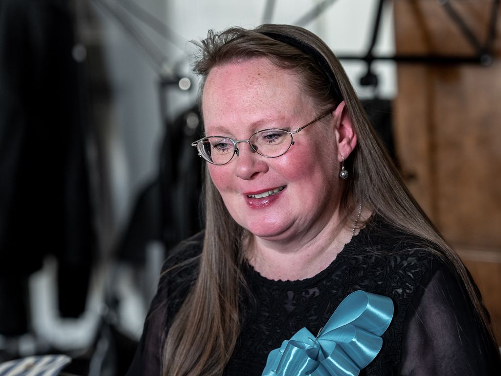 Punaposkinen nainen katsoo hymyillen alaspäin turkoosi rusetti rinnassaan