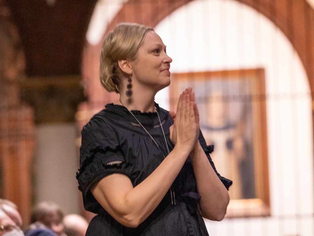 Kuoronjohtaja taittaa kädet yhteen hymyillen kirkossa