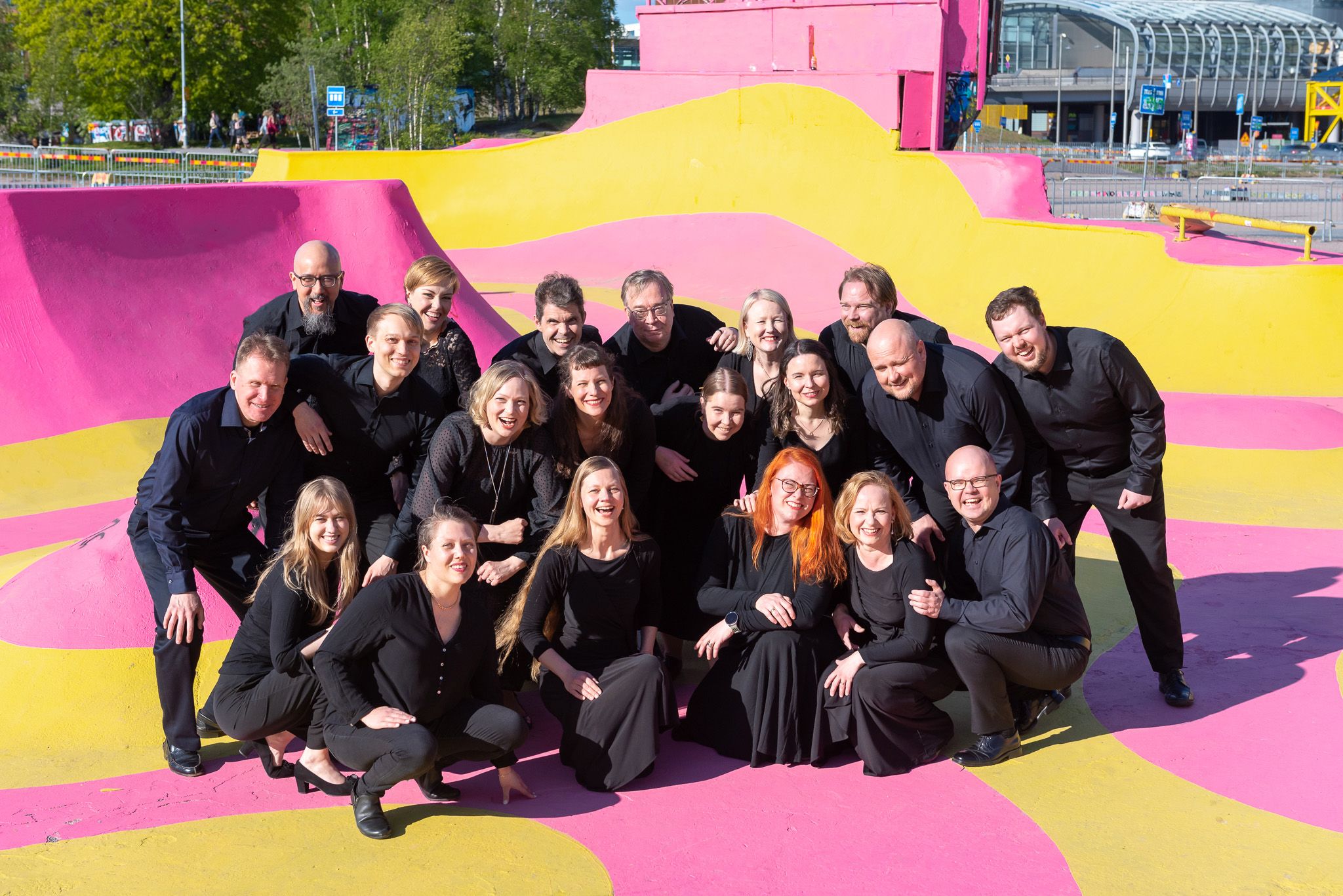 Kuorolaiset ryhmäkuvassa värikkään taustan edessä Kuorolaiset ryhmäkuvassa värikkään taustan edessä